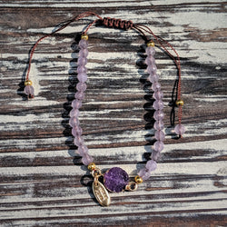 Purple crystal bracelet with silk cord and gold beads, displayed on rustic wood background.

