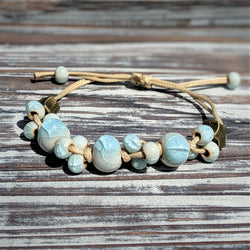 Sea Dreams bracelet with blue-toned ceramic glass beads on natural cord, styled flat on wooden background.