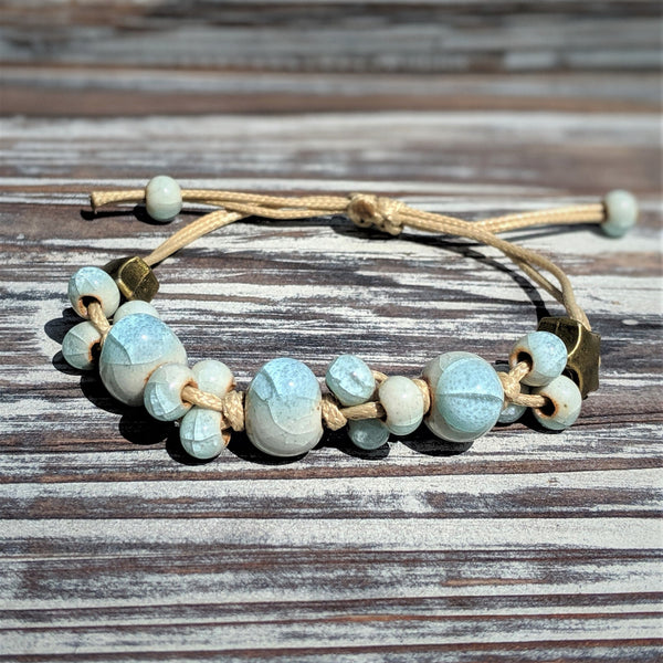 Sea Dreams bracelet with blue-toned ceramic glass beads on natural cord, styled flat on wooden background.