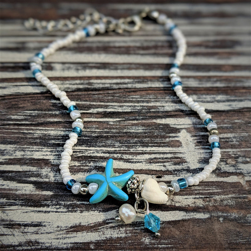  Starfish charm anklet with blue and white seed beads and shell accents, laid flat on wood background.