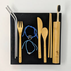 Eco-friendly gift set including bamboo toothbrush, metal straws, utensils, and bracelets in flat lay. Nymph Ki