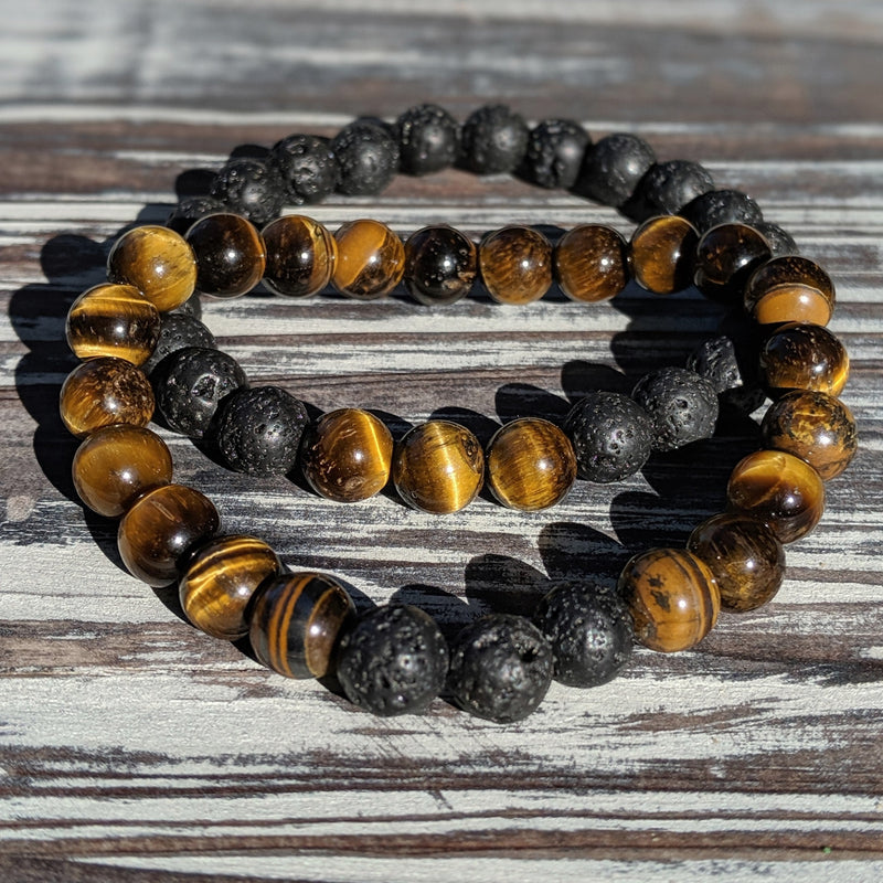Two stretch bracelets—one in Tiger’s Eye and one in Lava Rock—stacked together on rustic wood surface.