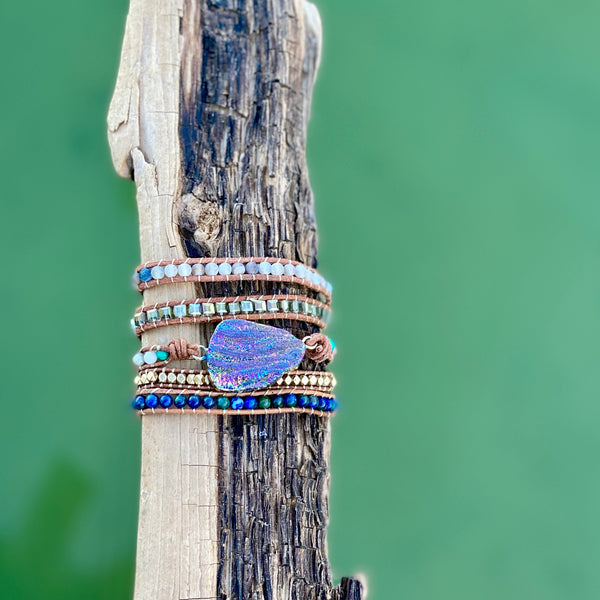 Rainbow Titanium Aura Quartz wrap bracelet with layered beads and shimmer detail over jewel green water.