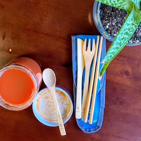 Bamboo cutlery set with chopsticks, spoon, fork, and knife in a navy cloth pouch, displayed with smoothie and grains.