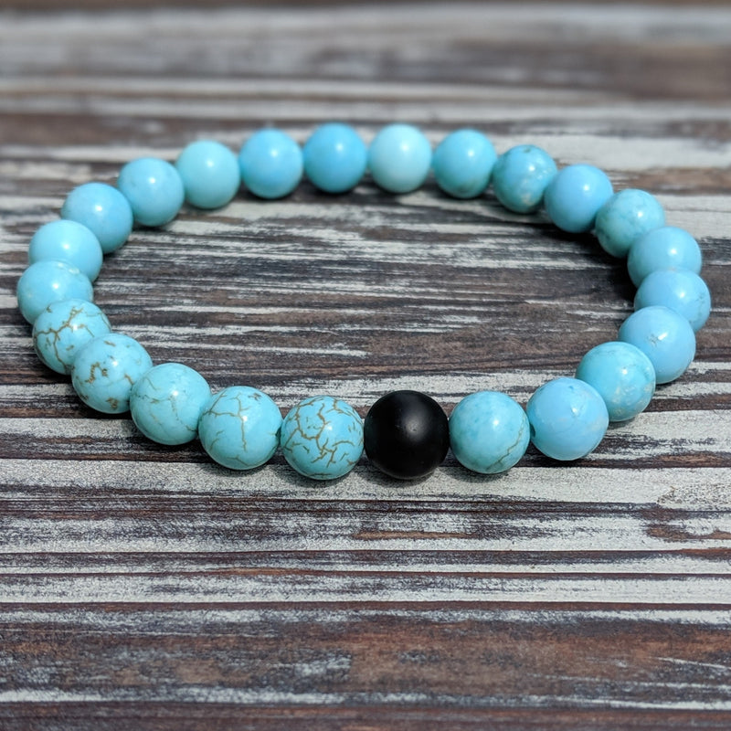 Turquoise beaded stretch bracelet displayed on wood with visible bead detail and cord flexibility.