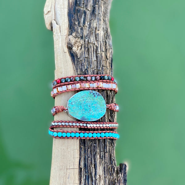 Turquoise crystal wrap bracelet displayed on driftwood with green background — handcrafted boho jewelry by Nymph Ki.