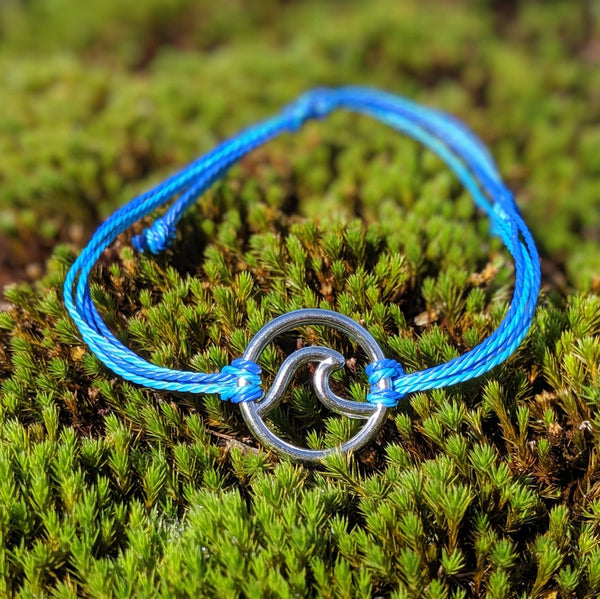 Silver wave charm bracelet with adjustable light and dark blue cords, displayed on moss background.

