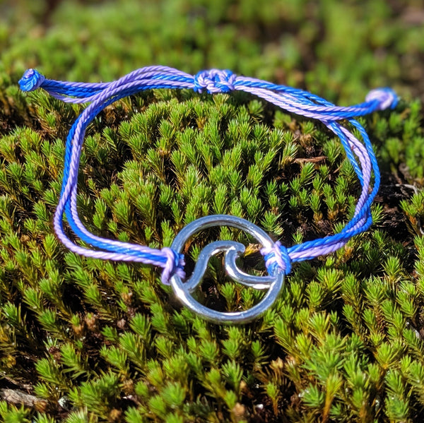Purple and blue adjustable cord bracelet with silver wave charm displayed on green moss.