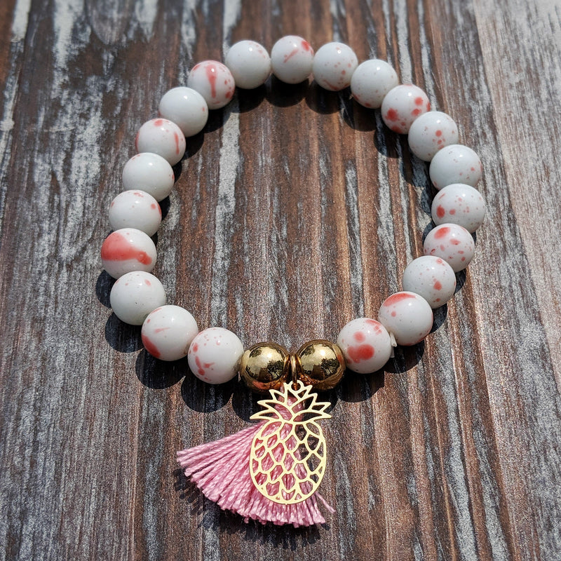 White and pink gemstone-style beaded bracelet with pink tassel charm.

